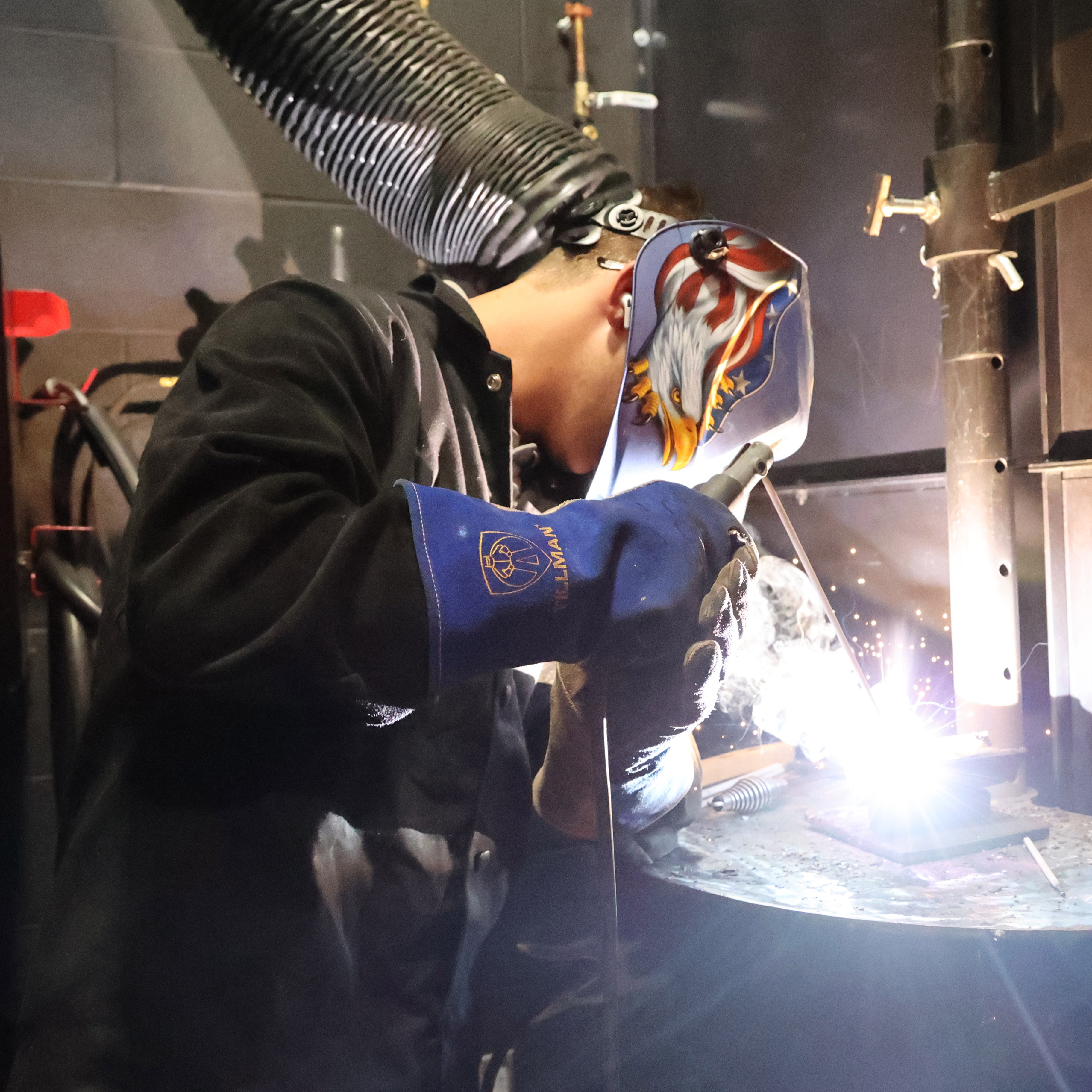 Student in a welding bay with his hood down and sparks flying