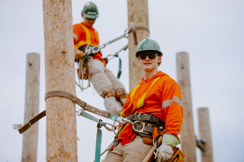 Two individuals with safety harnesses stationed between two electrical power poles.