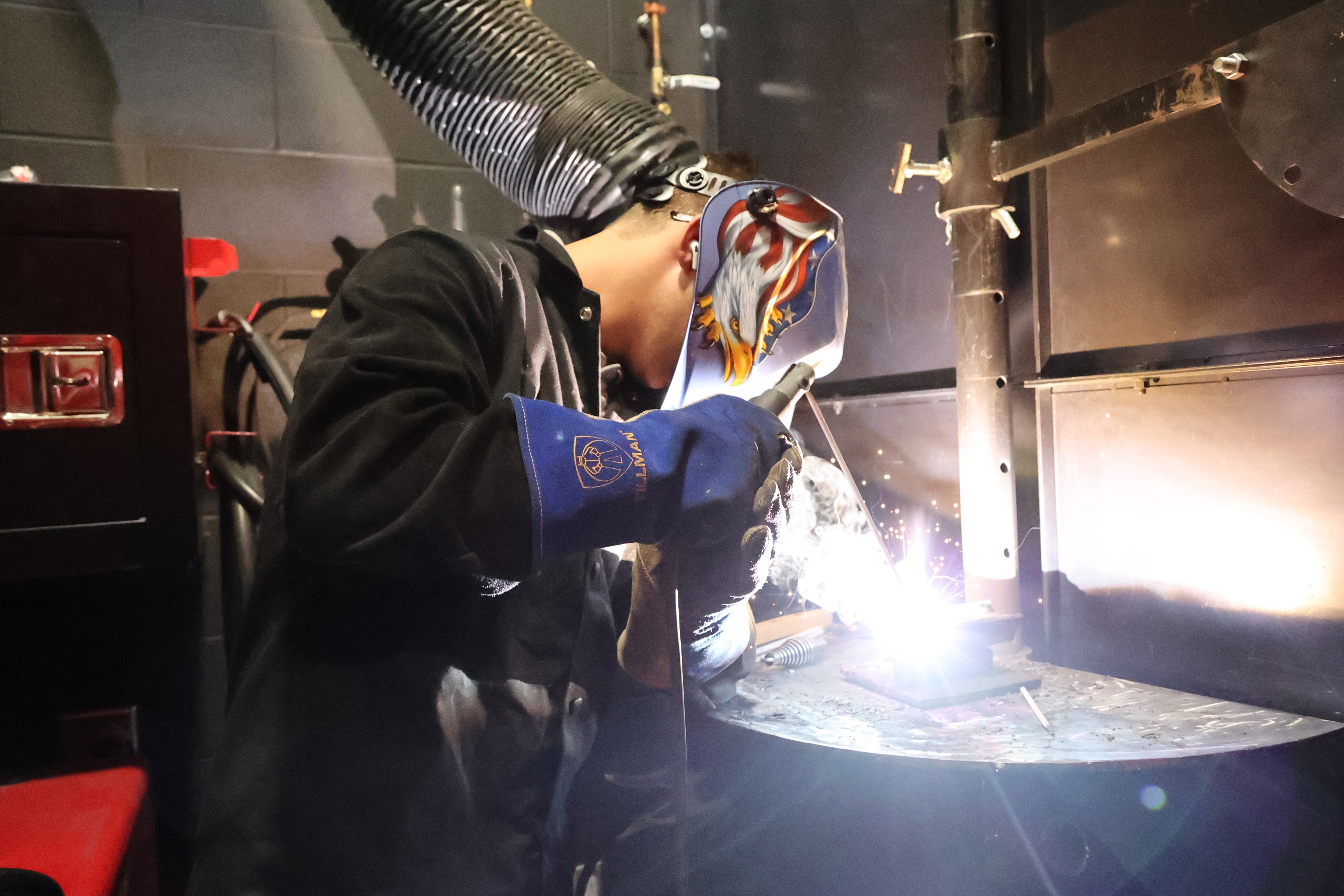 A male student has his welding wand touching metal and spewing flames and sparks.