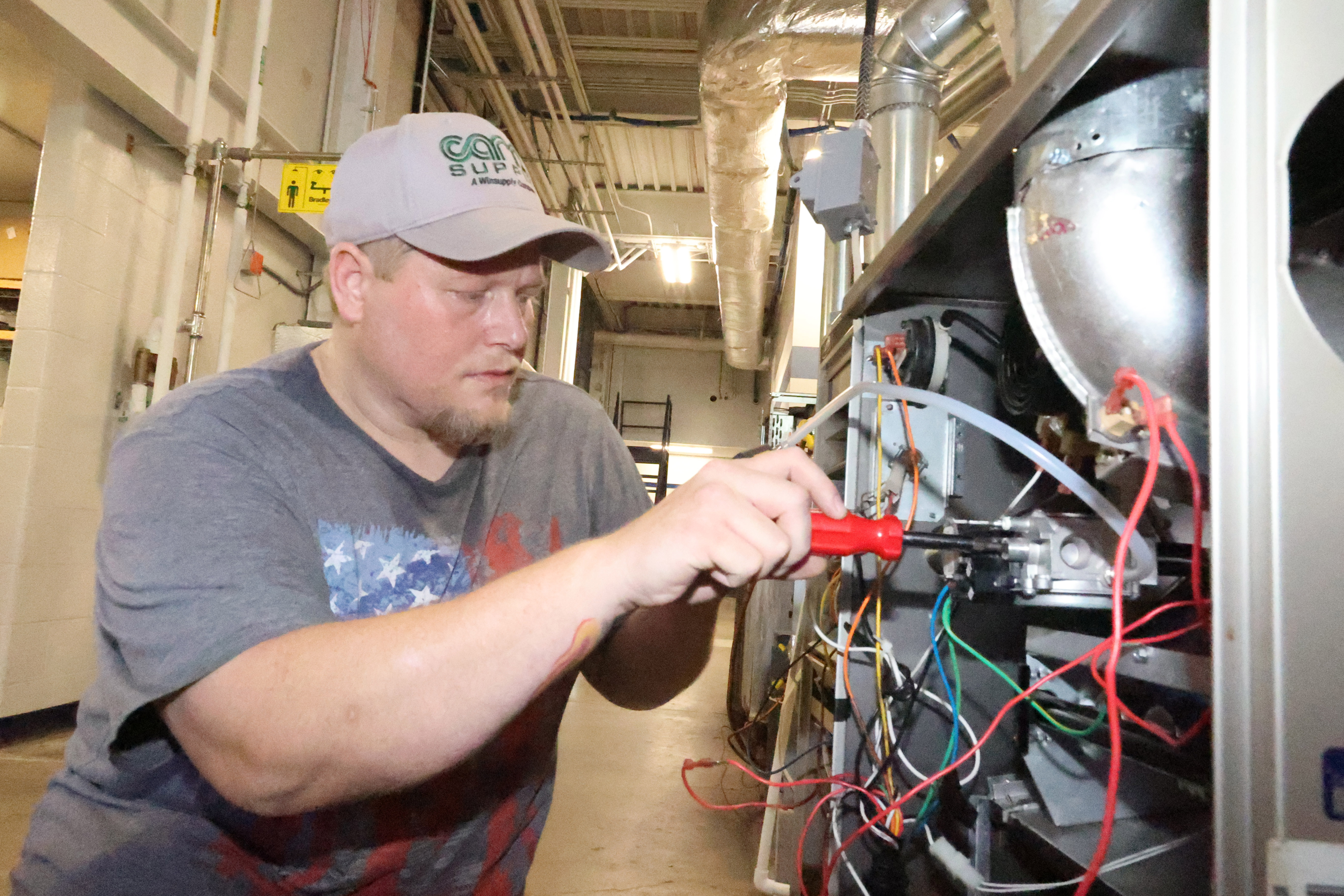 A White, male student lines up his screwdriver as he begins to prepare repairing an air conditioning unit.