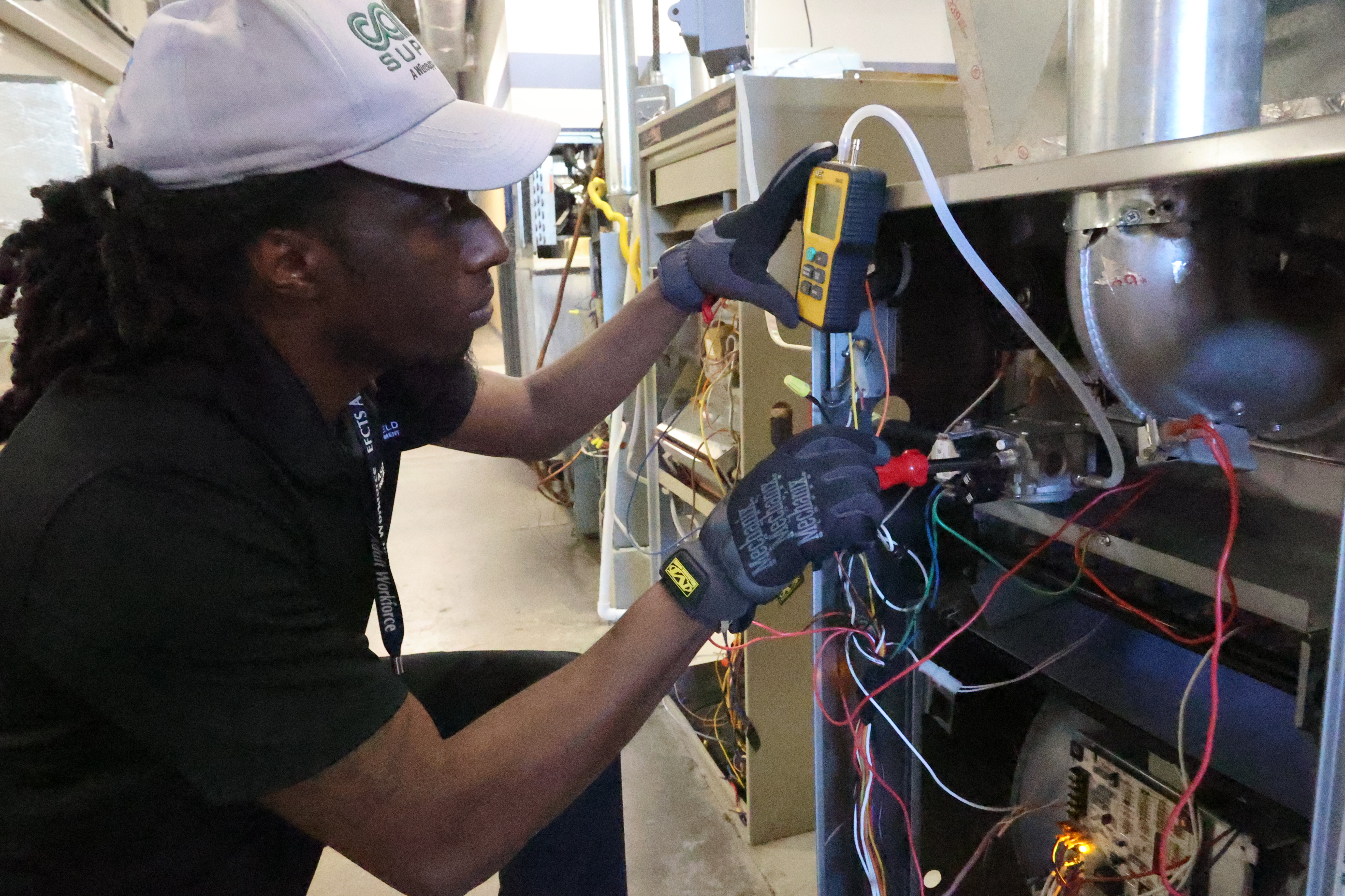 A Black, male student uses a red screwdriver to make adjustments to an AC unit.