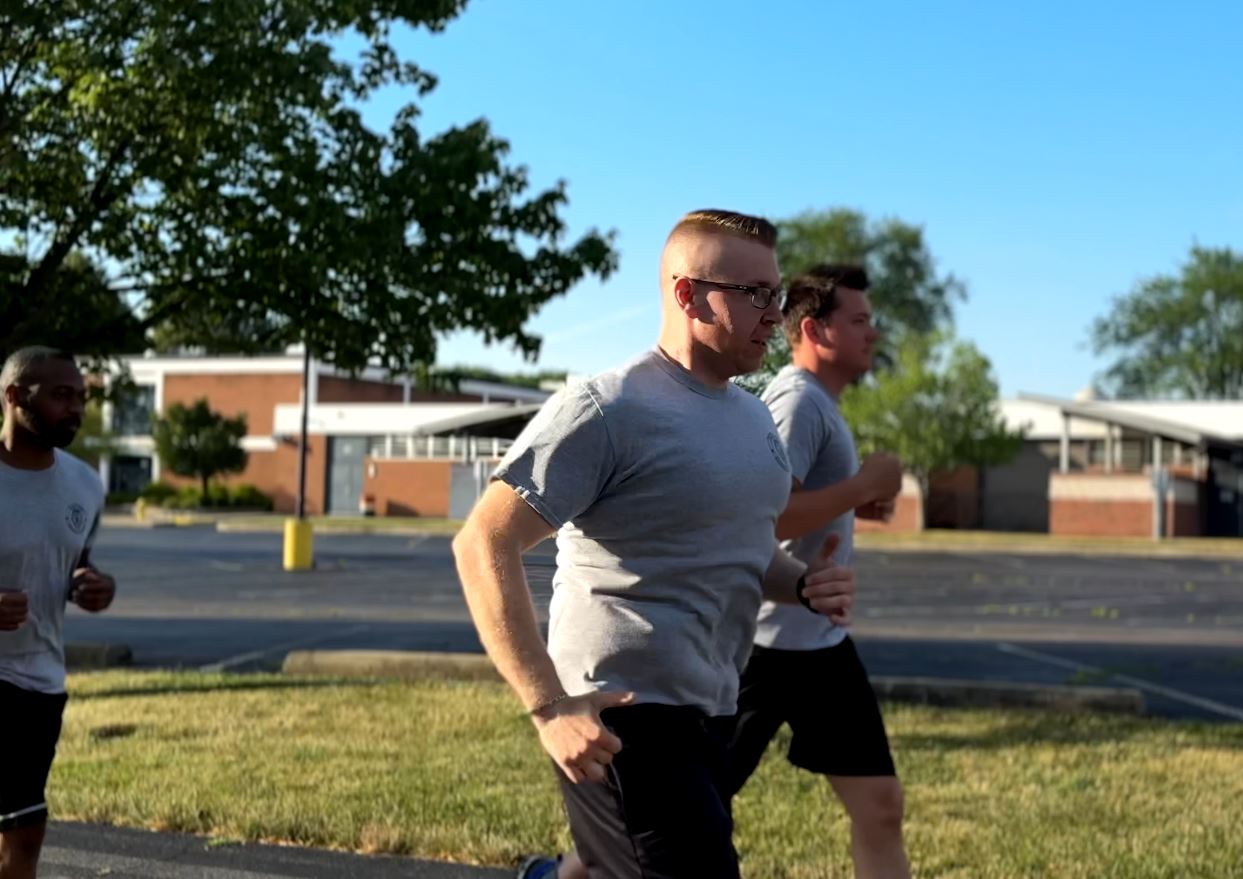 Three police cadets are running outside on a sunny morning.