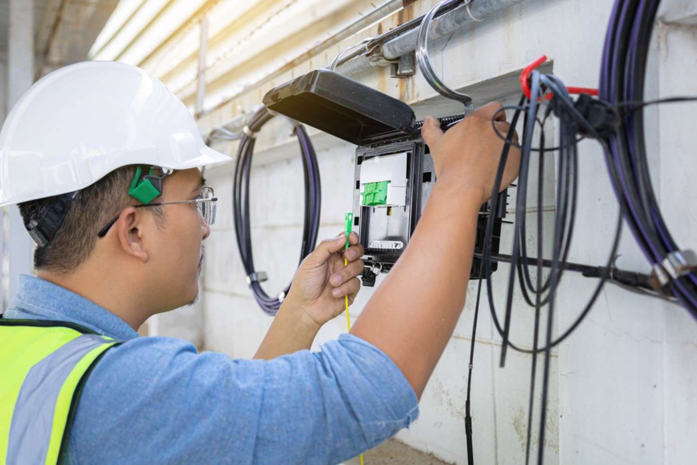 Man installing fiber optic on the side of a building.