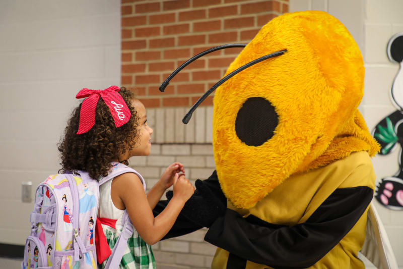 A young student holding hands with the yellow jacket mascot