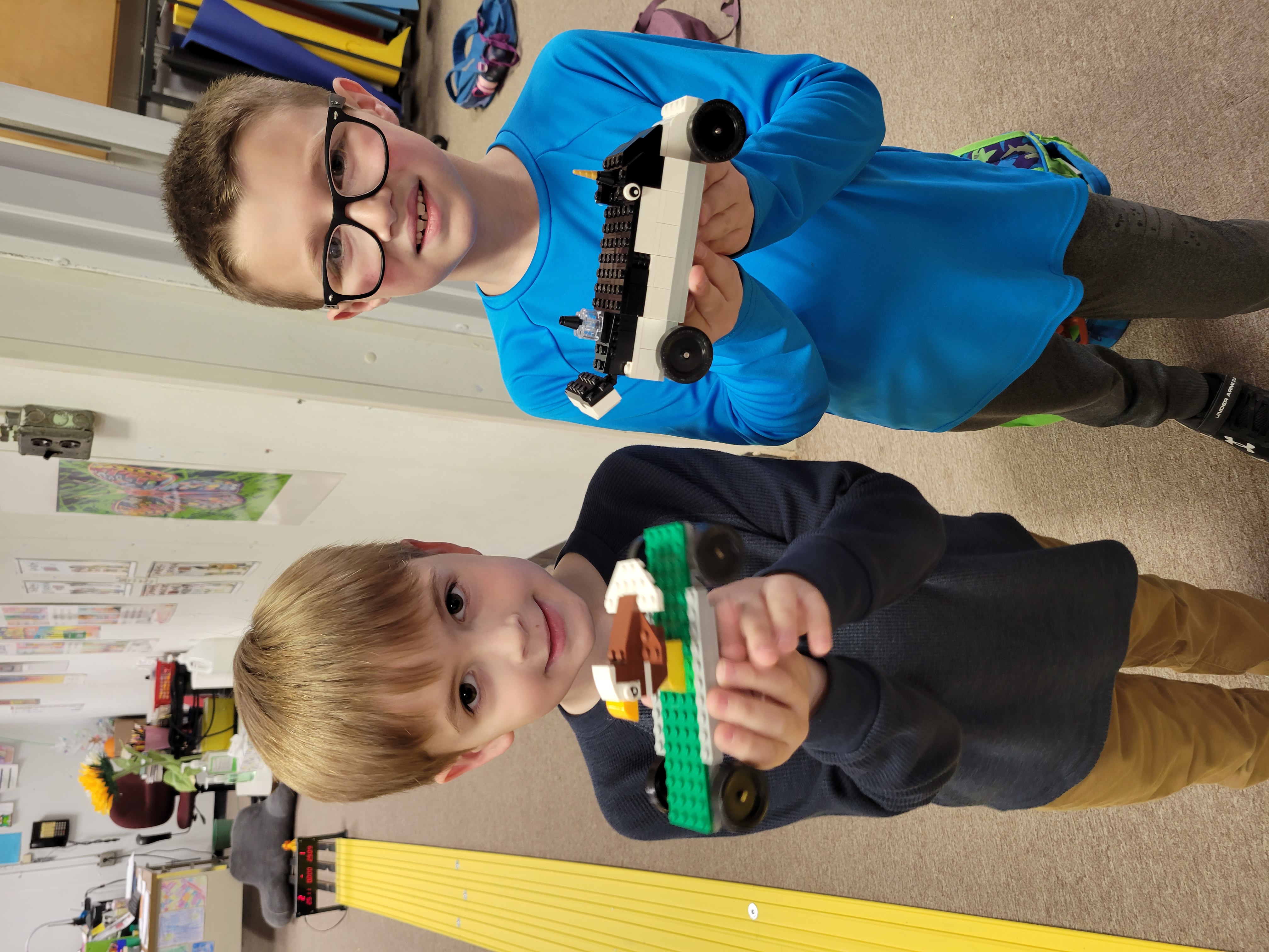 Two students hold the Lego cars they built. The students look proud and are smiling.