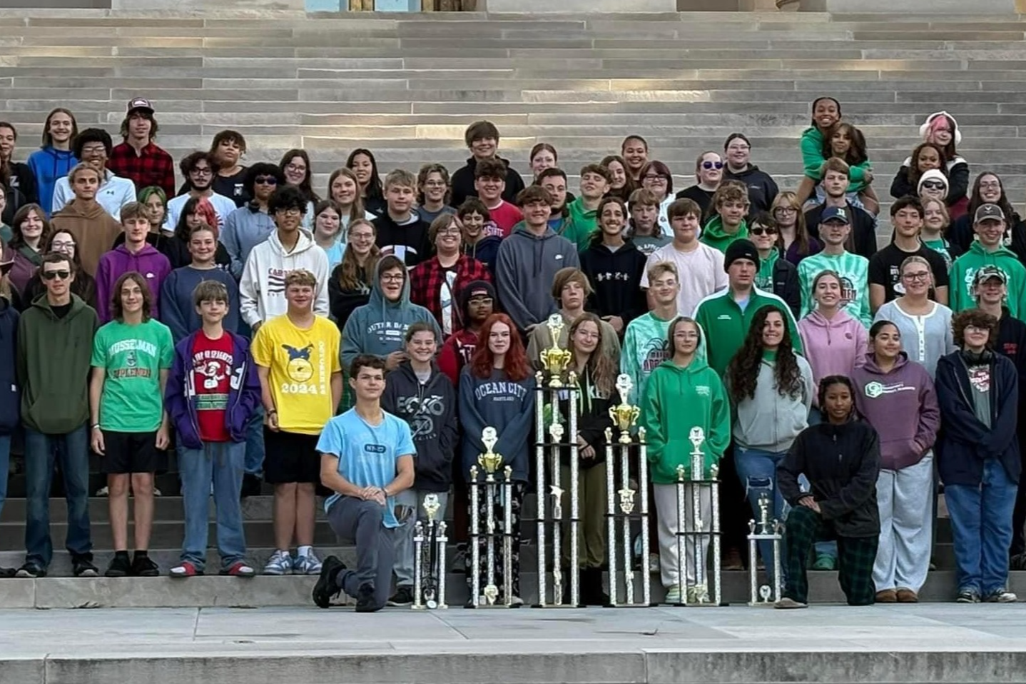 students with trophies in front of building