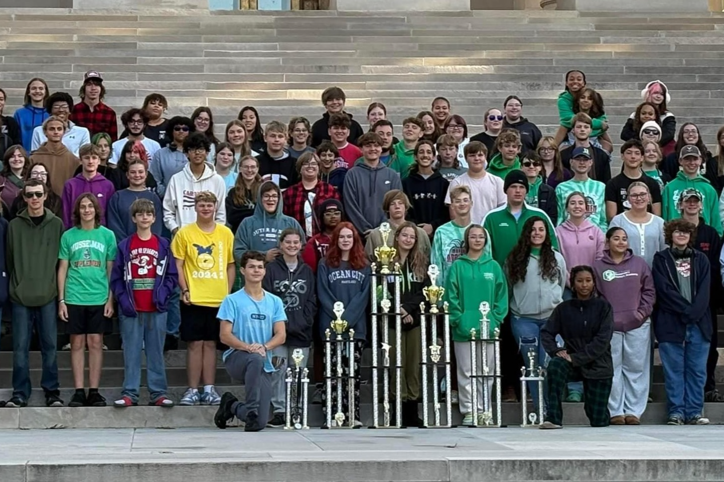 students with trophies in front of building