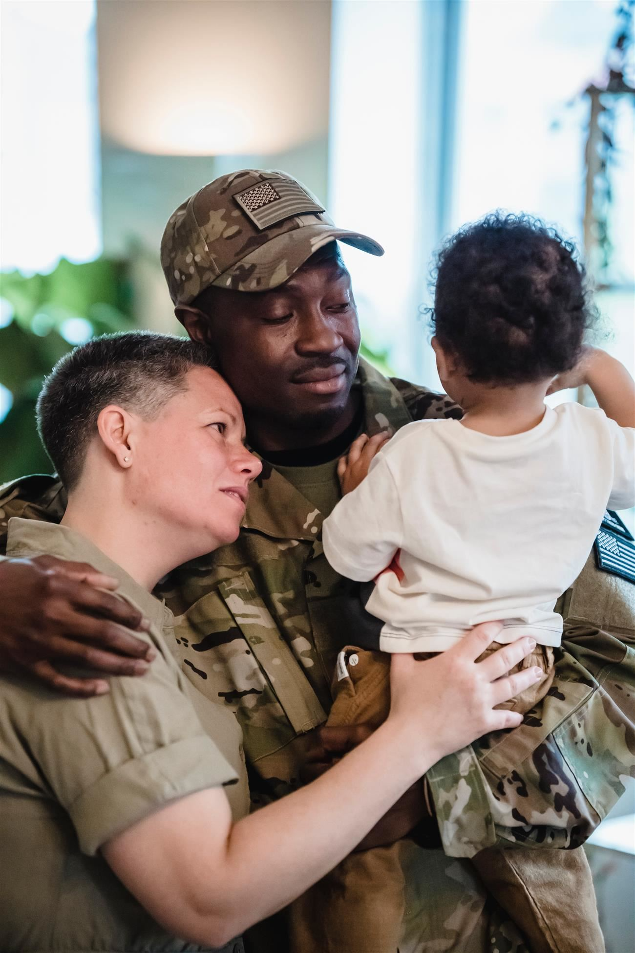 Military Man holding his child with one arm and embracing his partner with the other