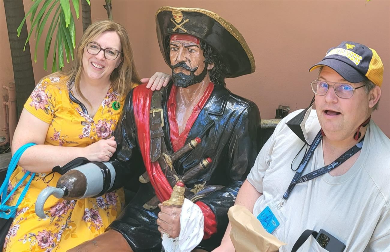 Two staff members take picture with pirate statue sitting down