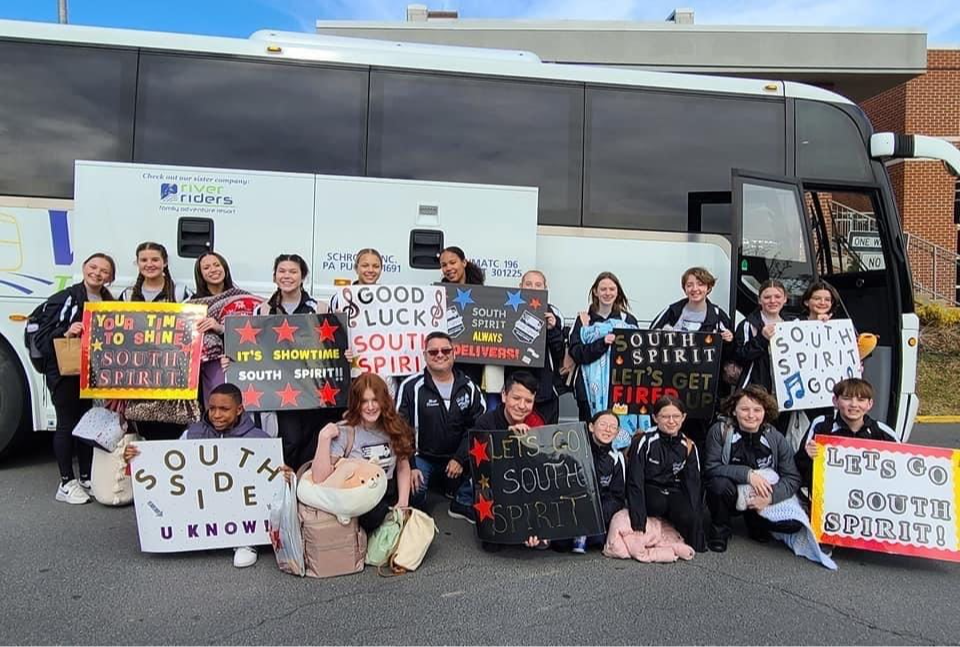 south spirit show choir students holding school spirit posters in front of bus
