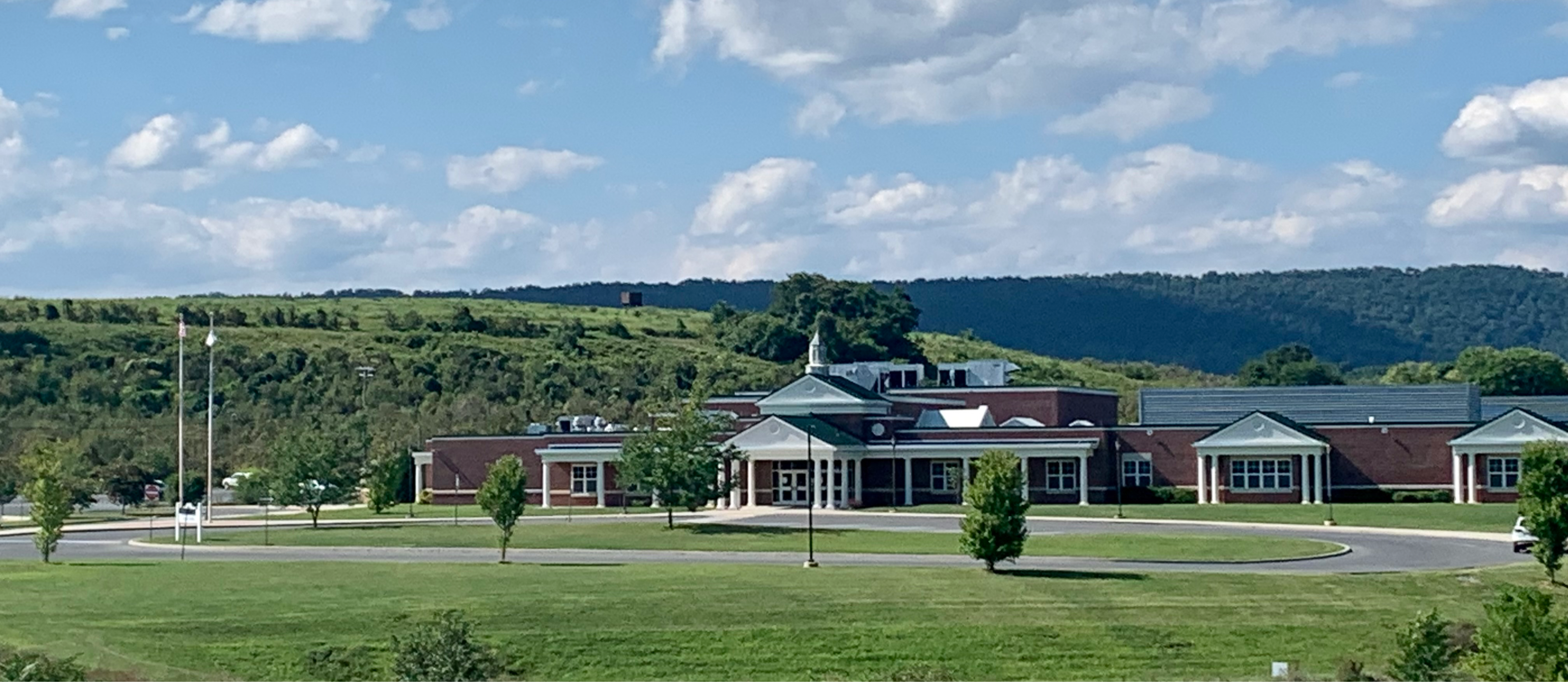 landscape picture of Mountain Ridge Middle brick building with lush green lawn and trees in foreground and blue sky and clouds in background