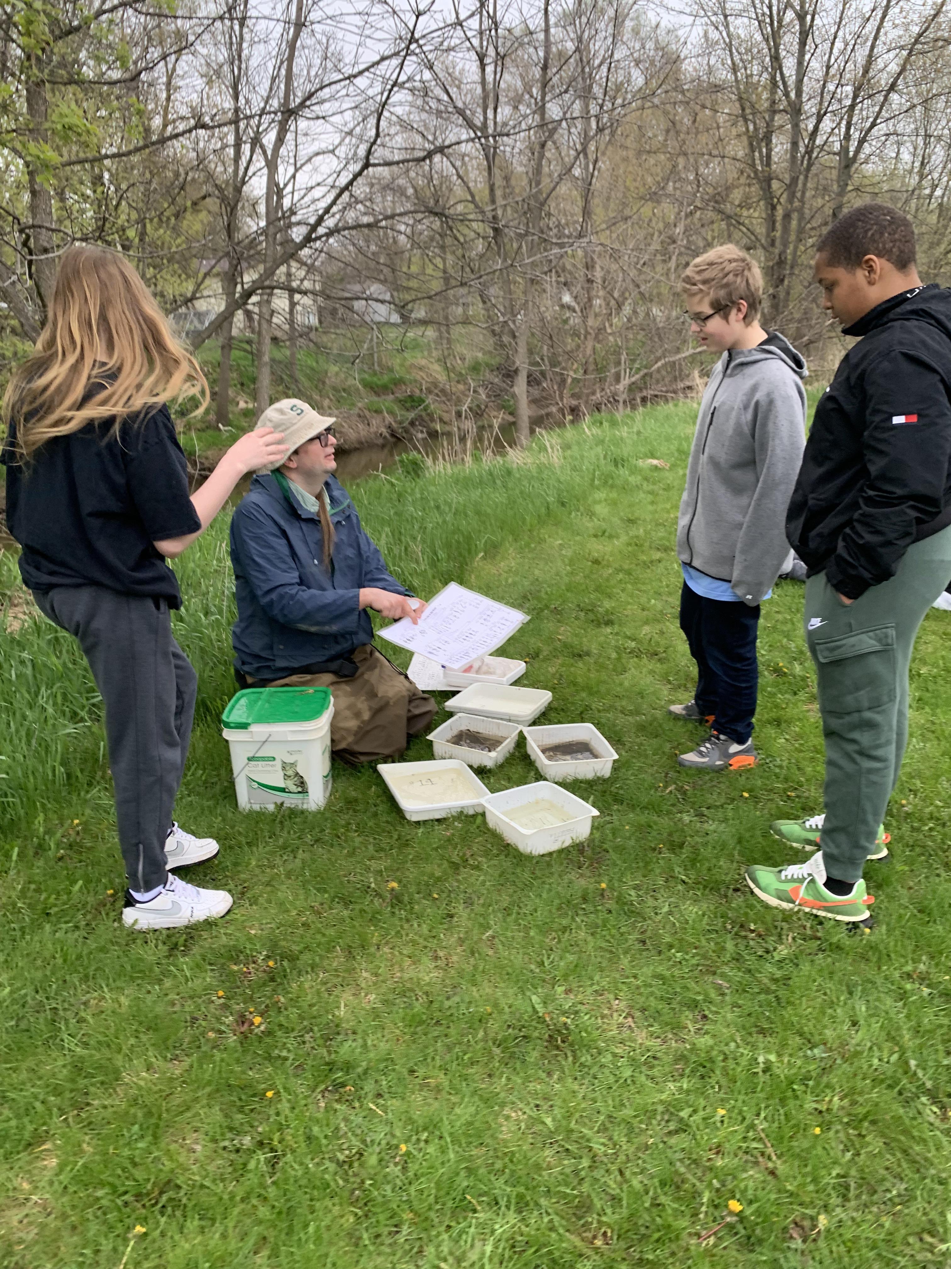 Students gathering around teacher at the creek