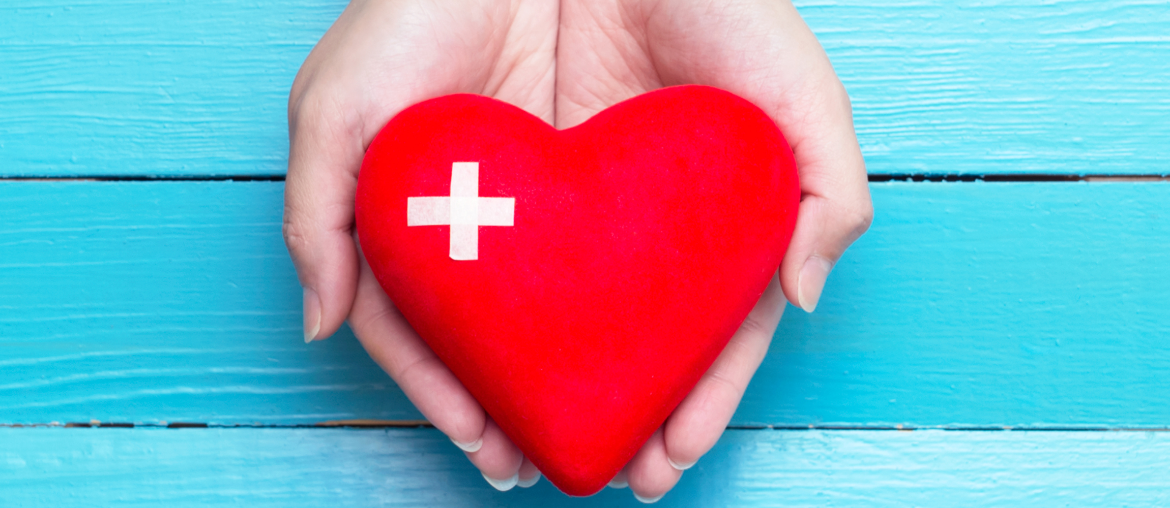 hands holding a red heart-shaped item with a white plus sign