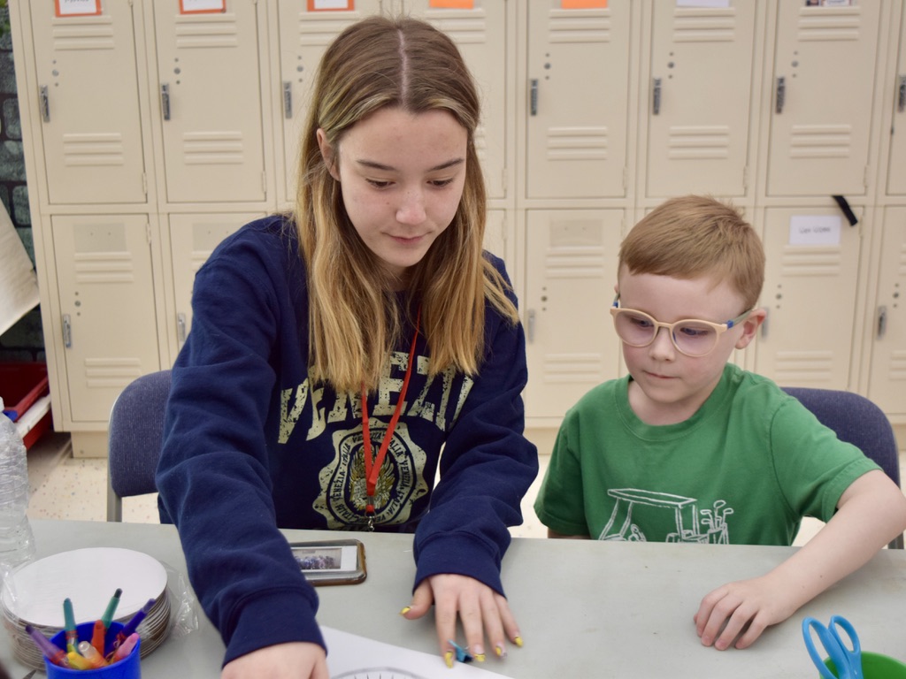 a teenage girl helps a young boy at a table