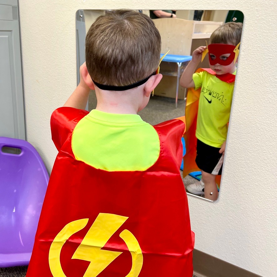 a small child wearing a cape and superhero mask looks at himself in a mirror