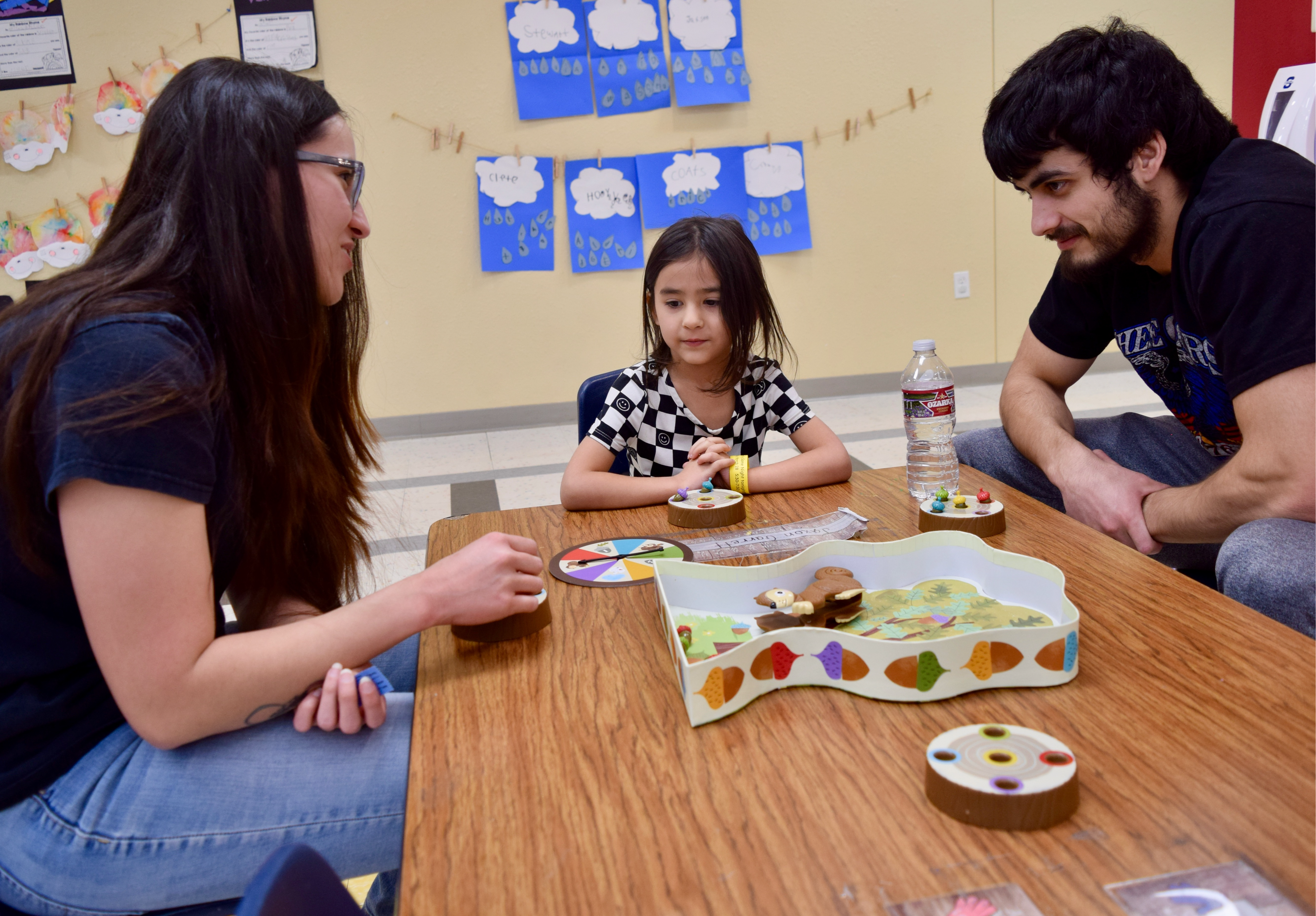 a child and a man and a woman play a board game while seated at a table