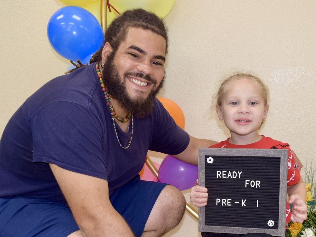 a father kneels next to his son holding a sign