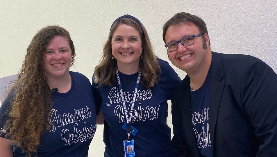 two women and a man wearing Shawnee Wolves navy blue t-shirts stand next to each other and smile