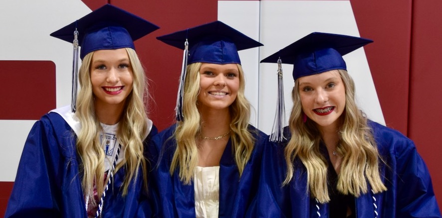 three girls wear blue graduation caps and gowns