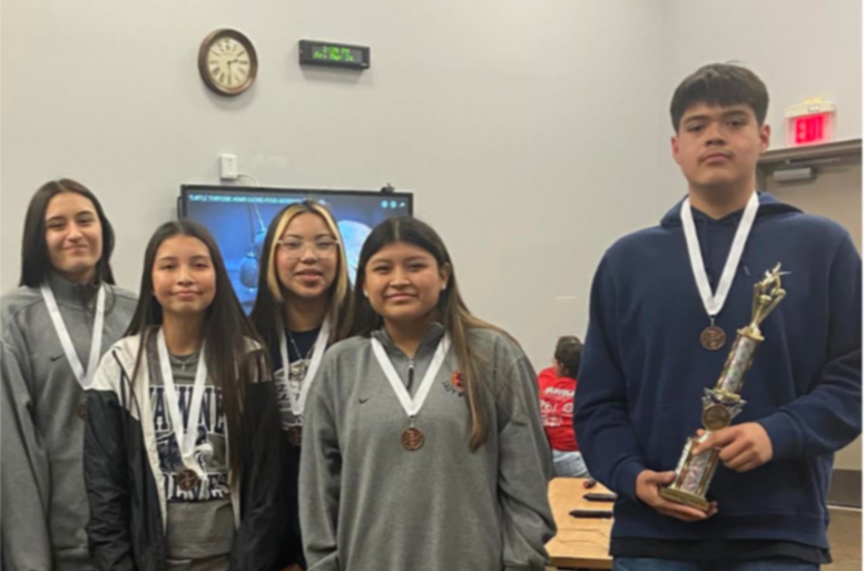 five students wearing medals stand next to each other. one holds a trophy