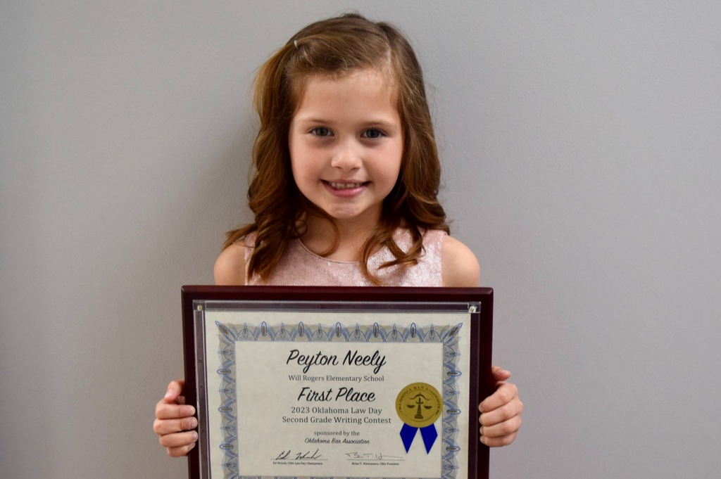 a girl wearing a pink dress holds a certificate reading first place