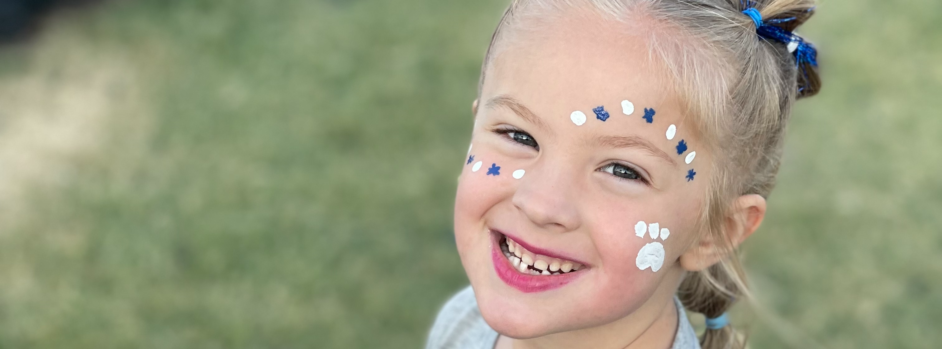 a smiling girl with blue and white pawprints painted on her face