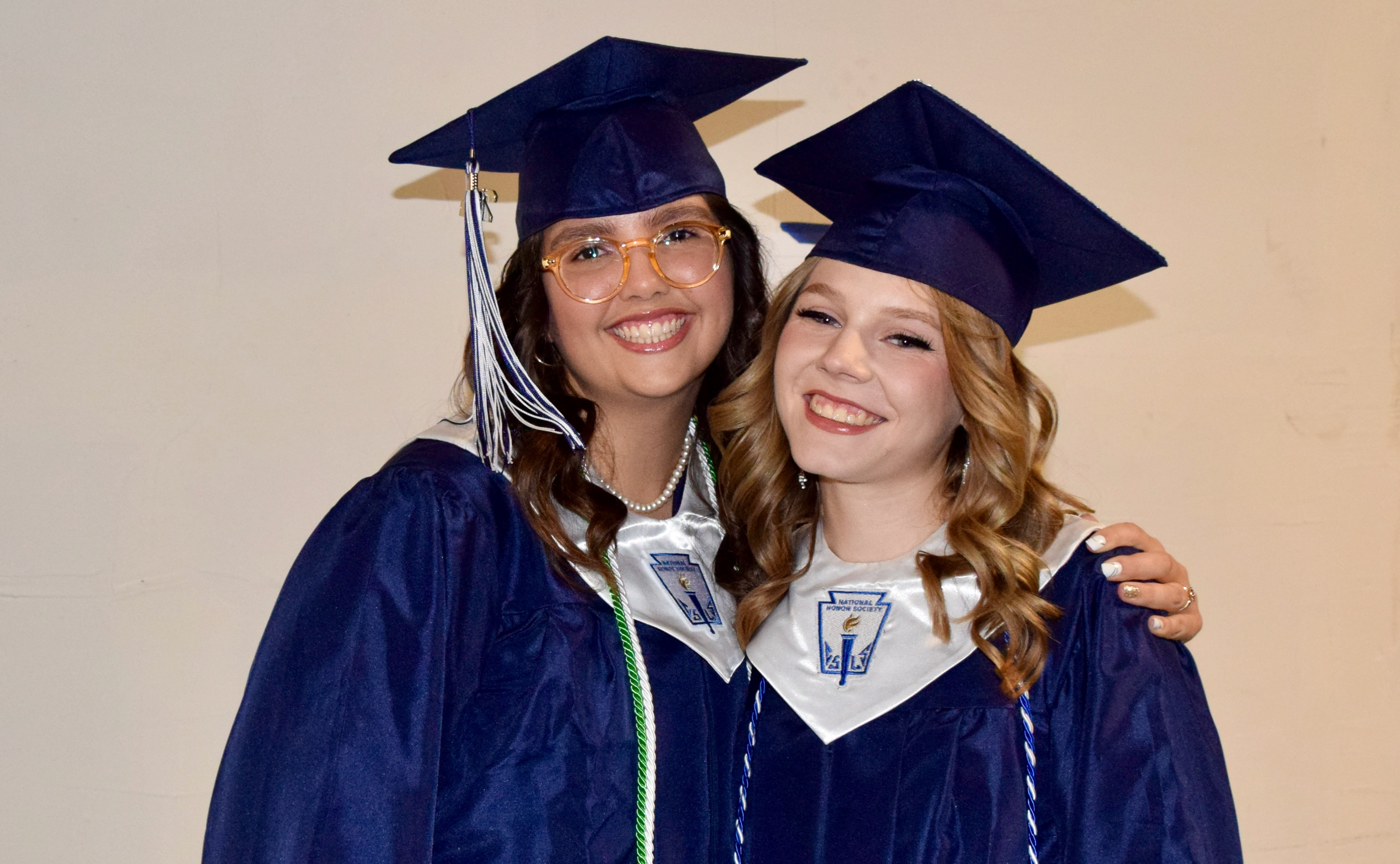 two girls wear blue graduation caps and gowns
