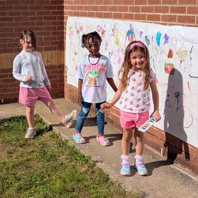 three PreK students painting banner outside