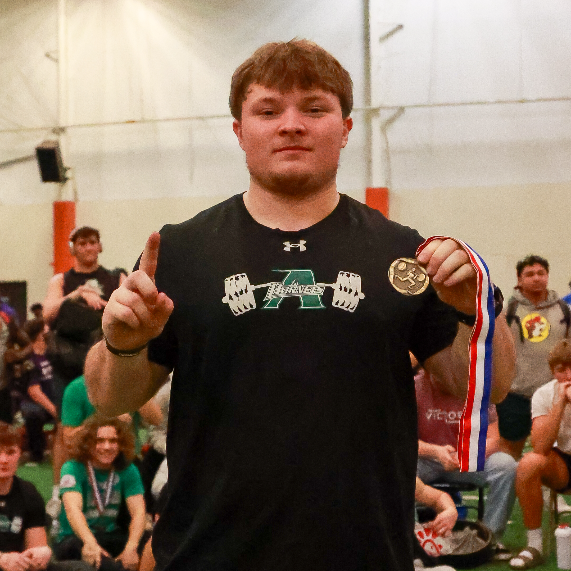 boy wearing black shirt, holding 1st place medal and one finger up