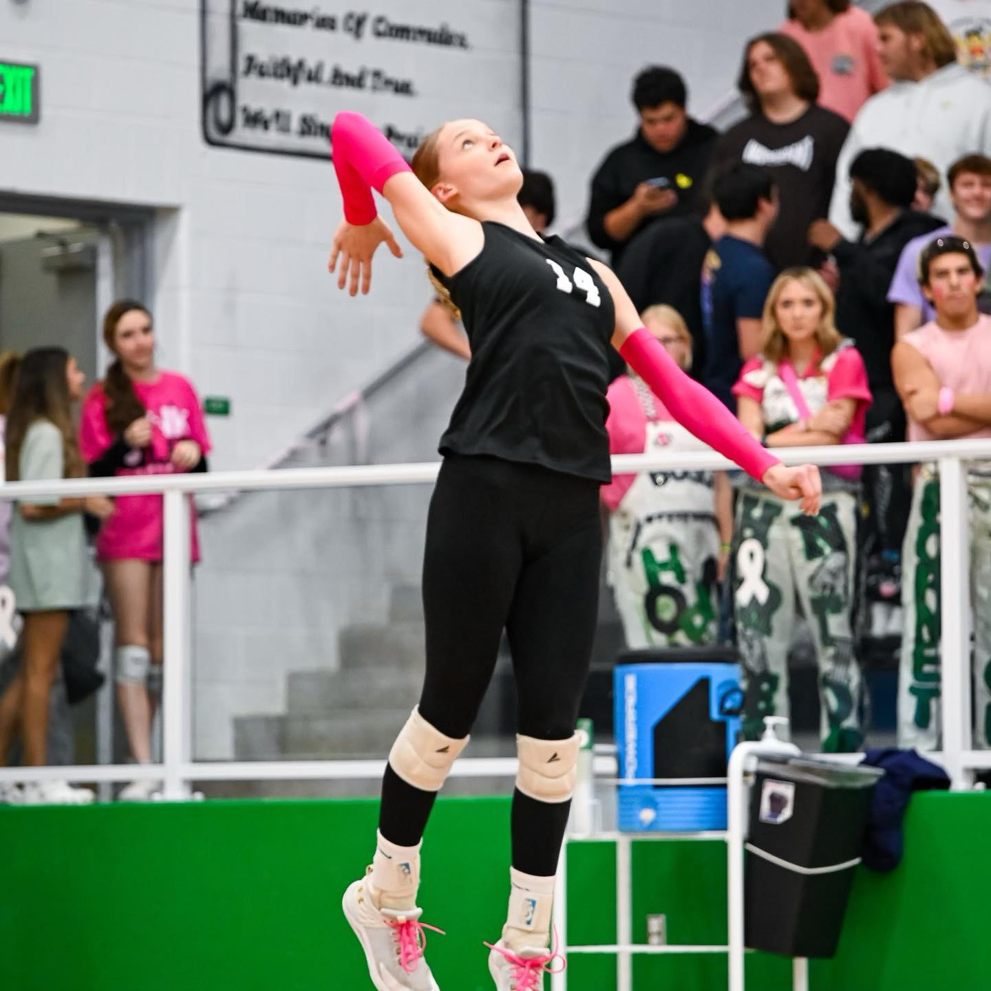 girl wearing black pants and shirt with pink arms, hitting volleyball