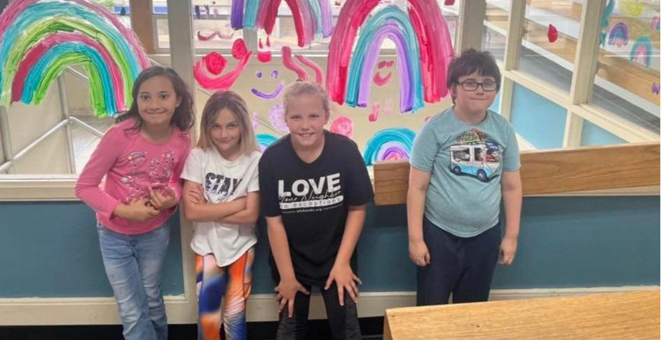 four students lined up against a window decorated with rainbows