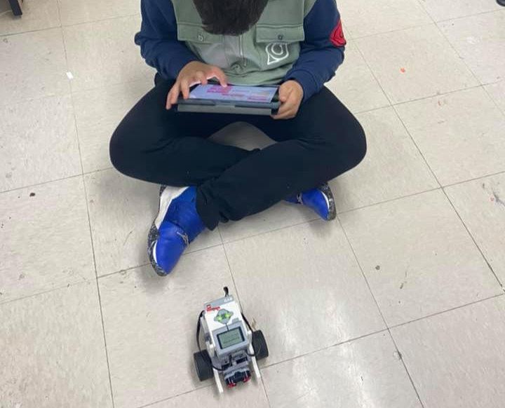 a boy uses an iPad to enter computer code for a robot in front of him