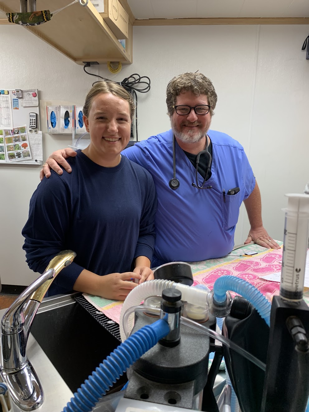 two smiling people stand behind medical equipment