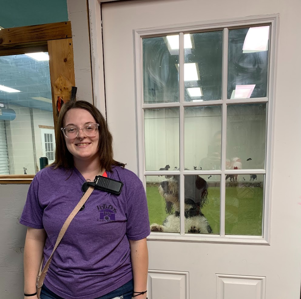 a young woman stands in front of a door with a dog peeking through the door's glass