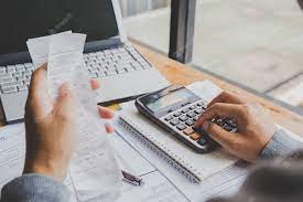 hand using calculator with receipts in other hand and laptop on table