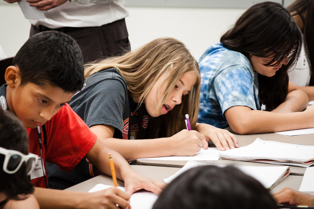 three students sitting at table writing in notebooks