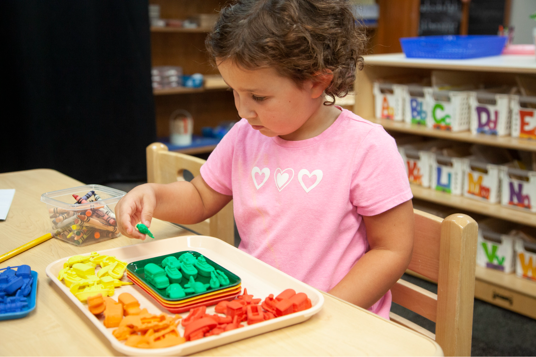 A small child, sorting out miniature vehicles by color into a tray.