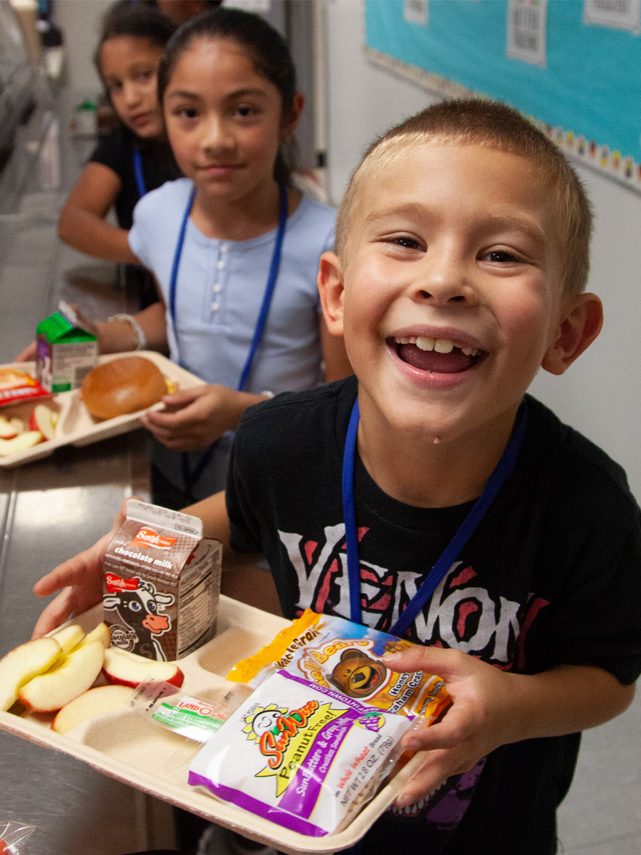 students in line in the cafeteria smiling after receiving a try of lunch food