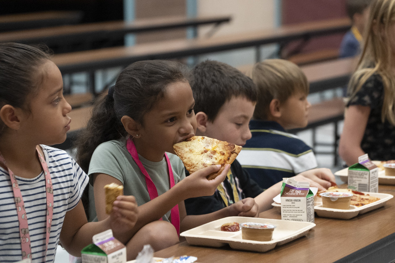 girls and boys eating pizza in the school cafeteria