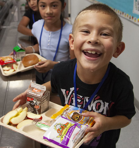 Smiling student holding a tray of lunch  items in the cafeteria standing in front of other students with lunch trays