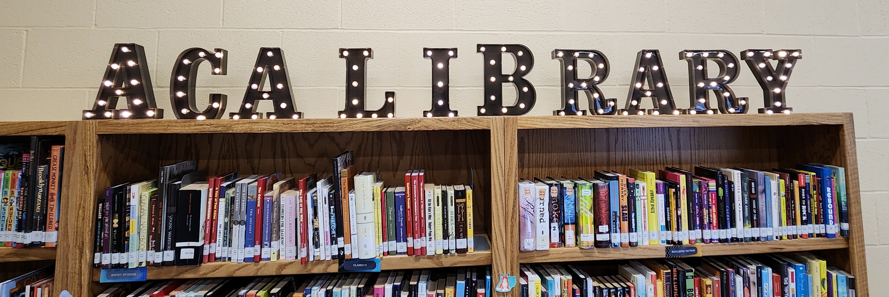 Lit up letters spell "ACA LIBRARY" on a bookshelf with books