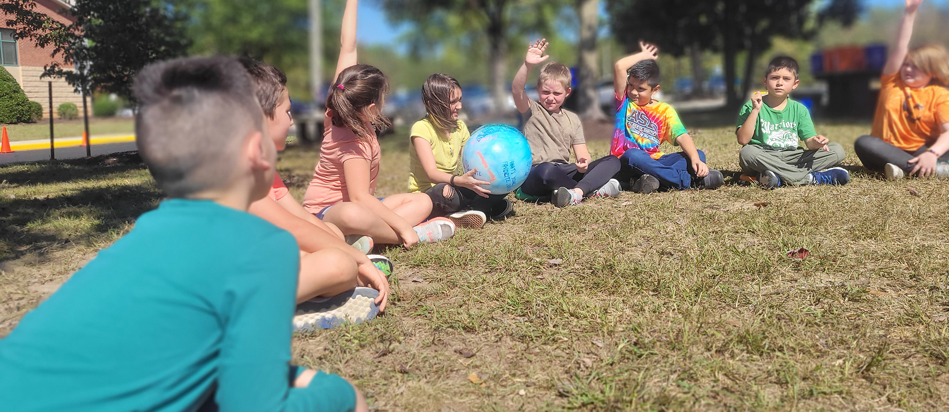 Group of young students sitting on the grass passing a blowup glob ball. 
