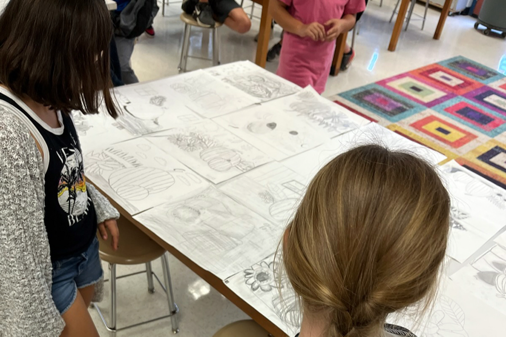 Two students looking at artwork spread out on a table
