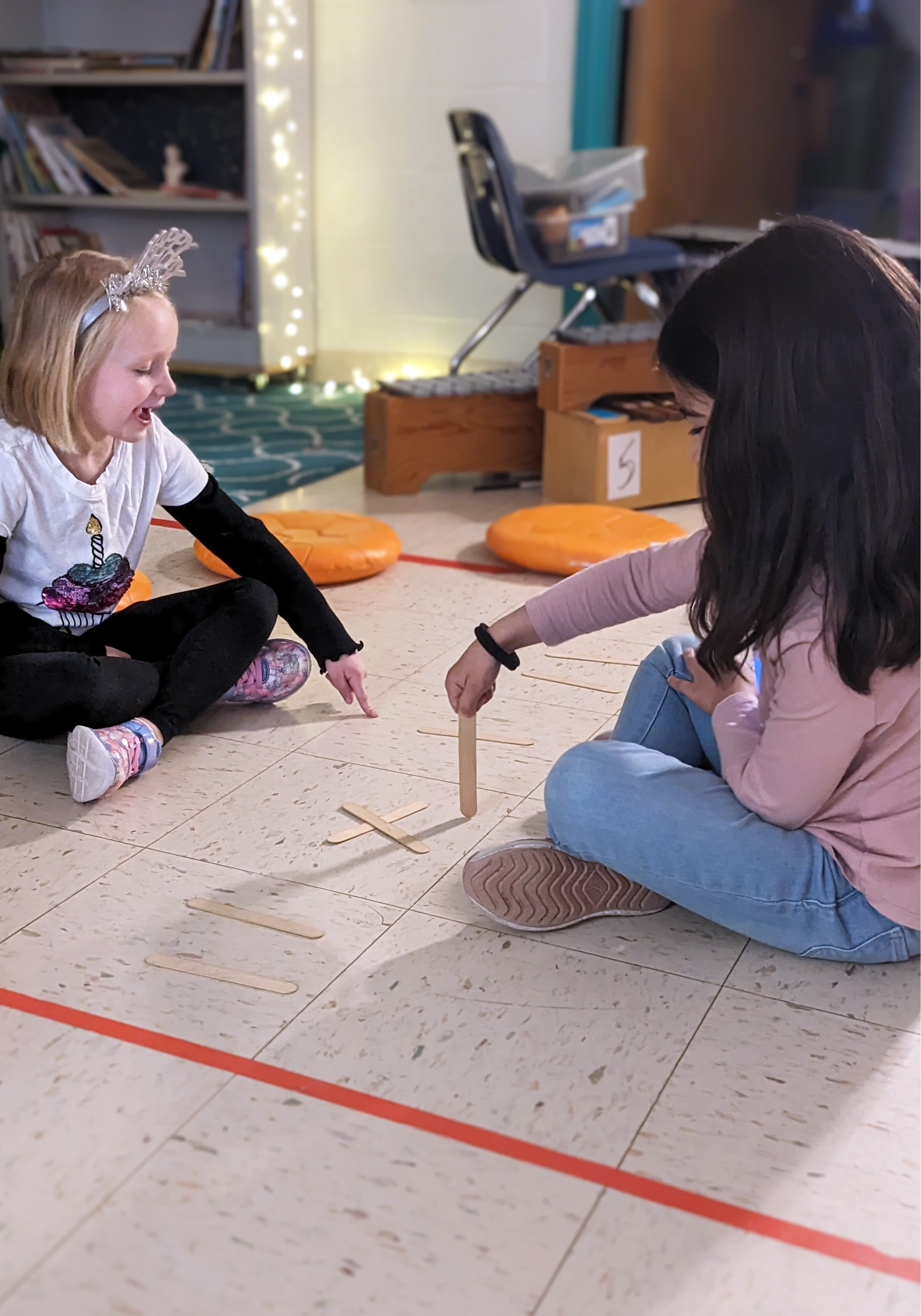 Two female students sitting on the floor working with pick up sticks.