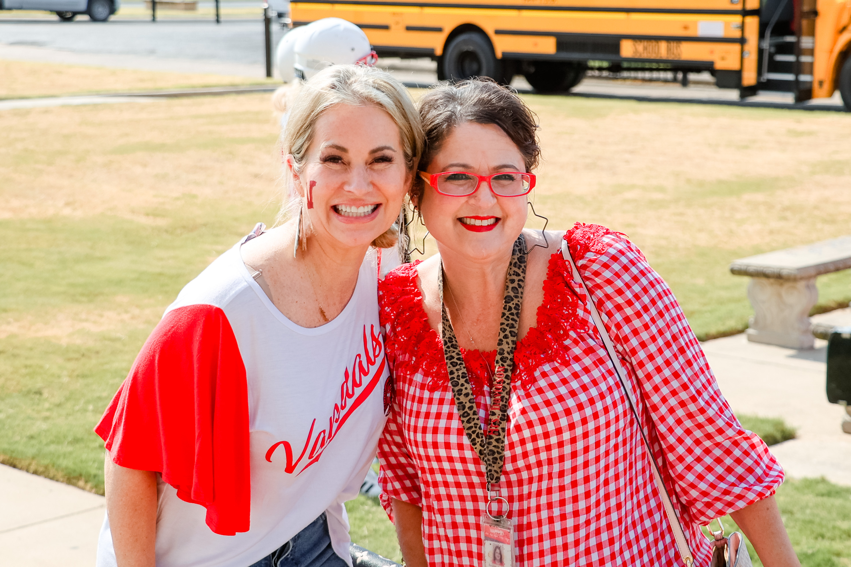 two teachers smile together for a photo in front of a school bus