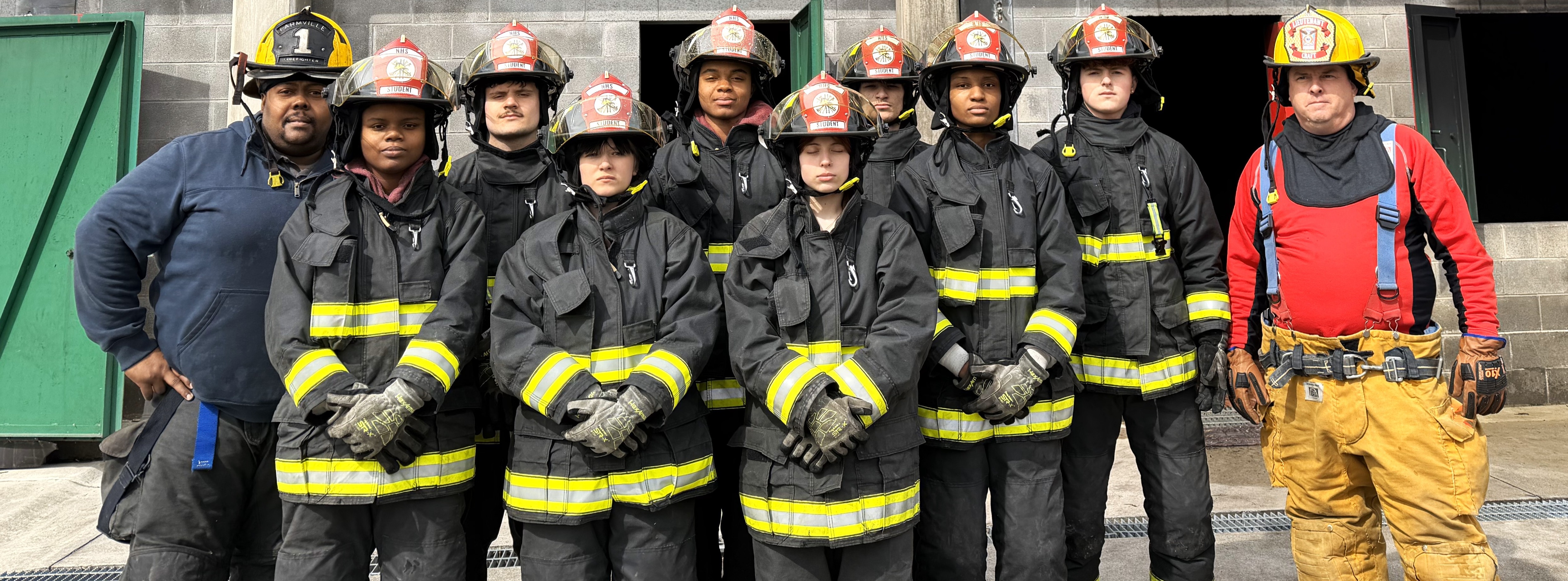 Group of firefighters in full uniform pose for a photo in front of a building.