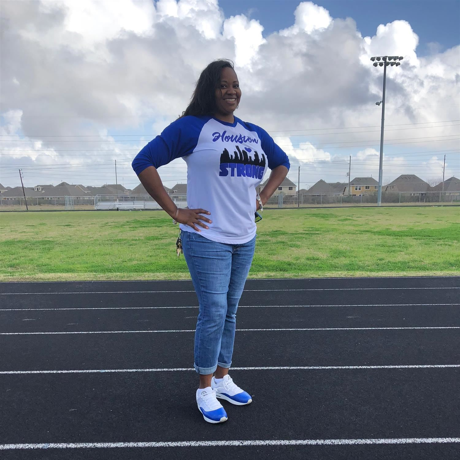 Shyron Richard-Johnson standing and smiling on the track outside wearing a houston strong shirt and jeans
