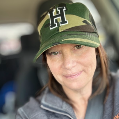 Gina Innacelli smiling wearing a camouflage hat in the selfie 
