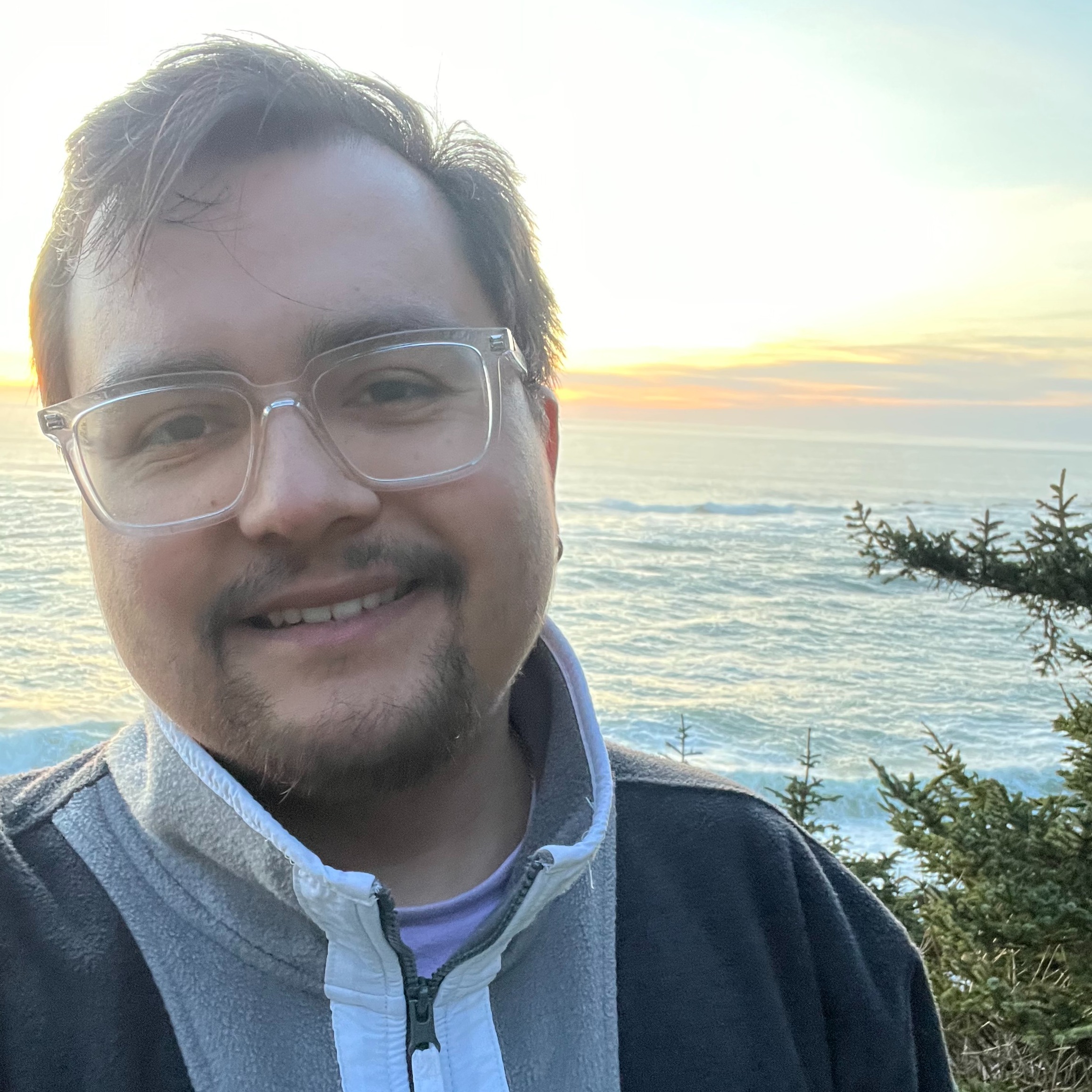 Christian Guerrero selfie in front of the water smiling wearing glasses and a hoodie