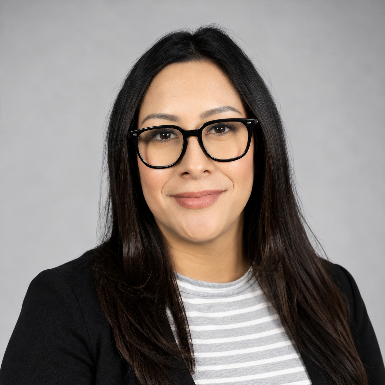 Professional headshot of Ms. Padilla, Science Instructional Support Teacher (IST) at Anthony Aguirre Junior High. She is smiling and wearing a black blazer over a gray-and-white striped blouse. She has long, straight dark hair, black-framed glasses, and is photographed against a light gray background.
